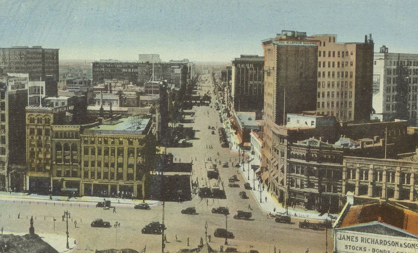 Tinted postcard of a wide downtown street with office blocks, cars and streetcars